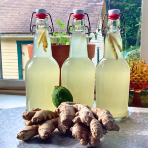 Three swing top bottles full of ginger beer with ginger and lime laying next to them