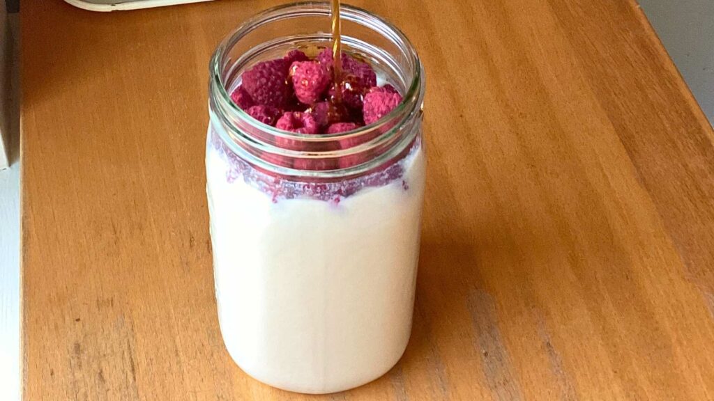 Mason jar full of kefir topped with freeze-dried raspberries and real maple syrup.