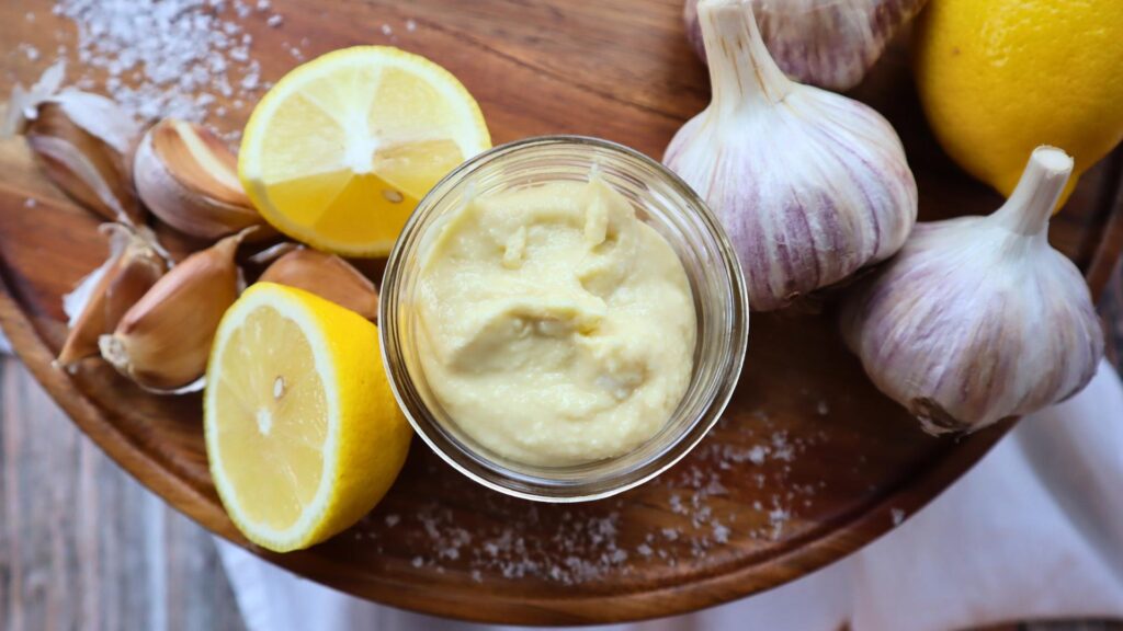 Garlic, lemons and salt with jar of fresh garlic toum.