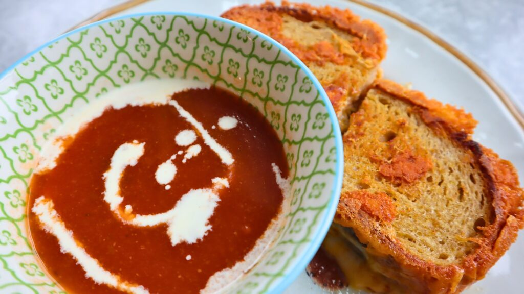 Closeup of crusty sourdough grilled cheese and tomato soup with cream on top.