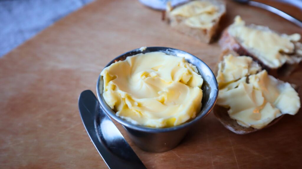 Small dish filled with cultured butter and sliced sourdough with cultured butter spread on.